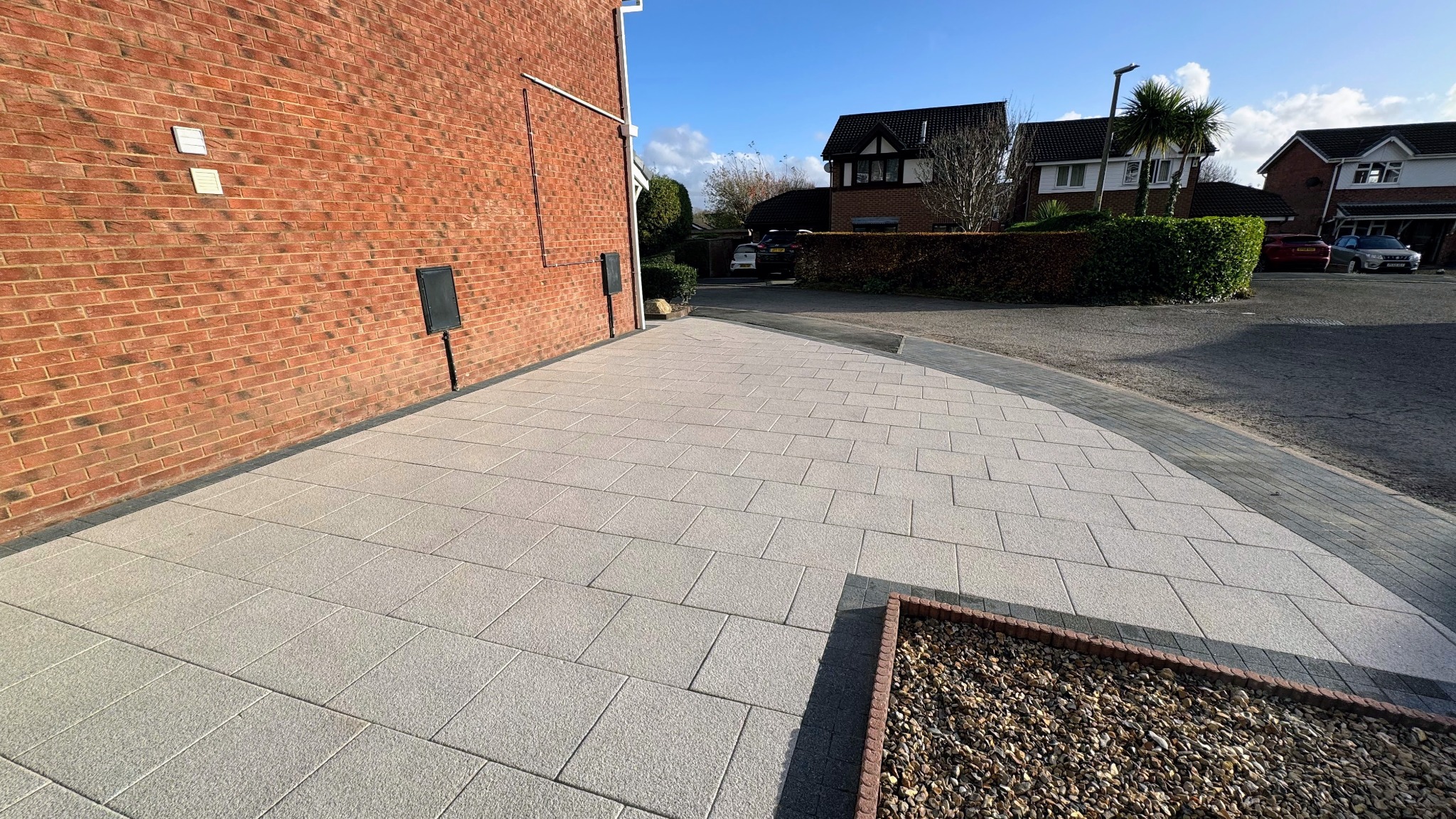 Light grey paved driveway with contrasting dark edging beside a brick house