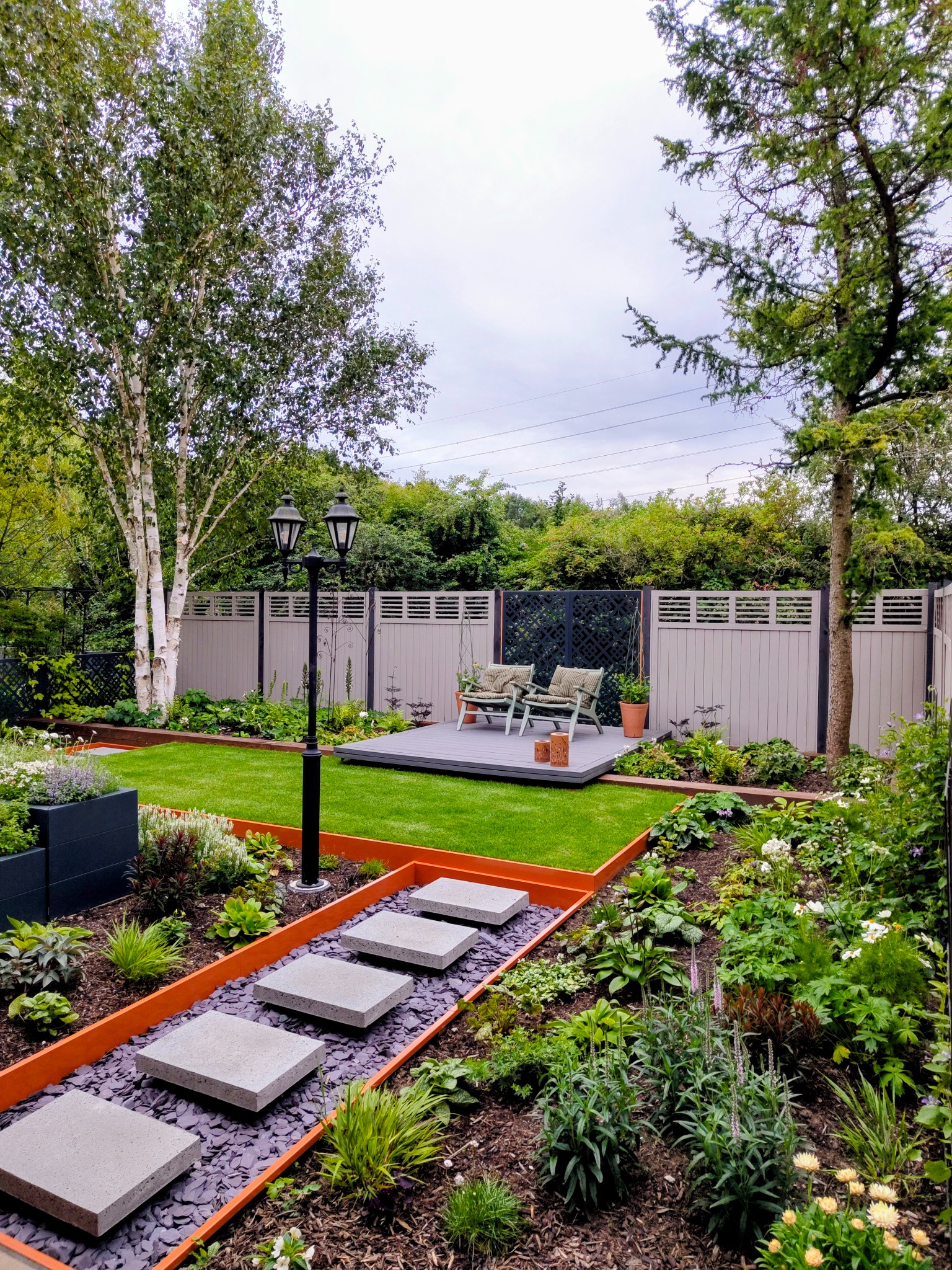 Garden with stepping stones, lush planting, lawn and a raised seating deck