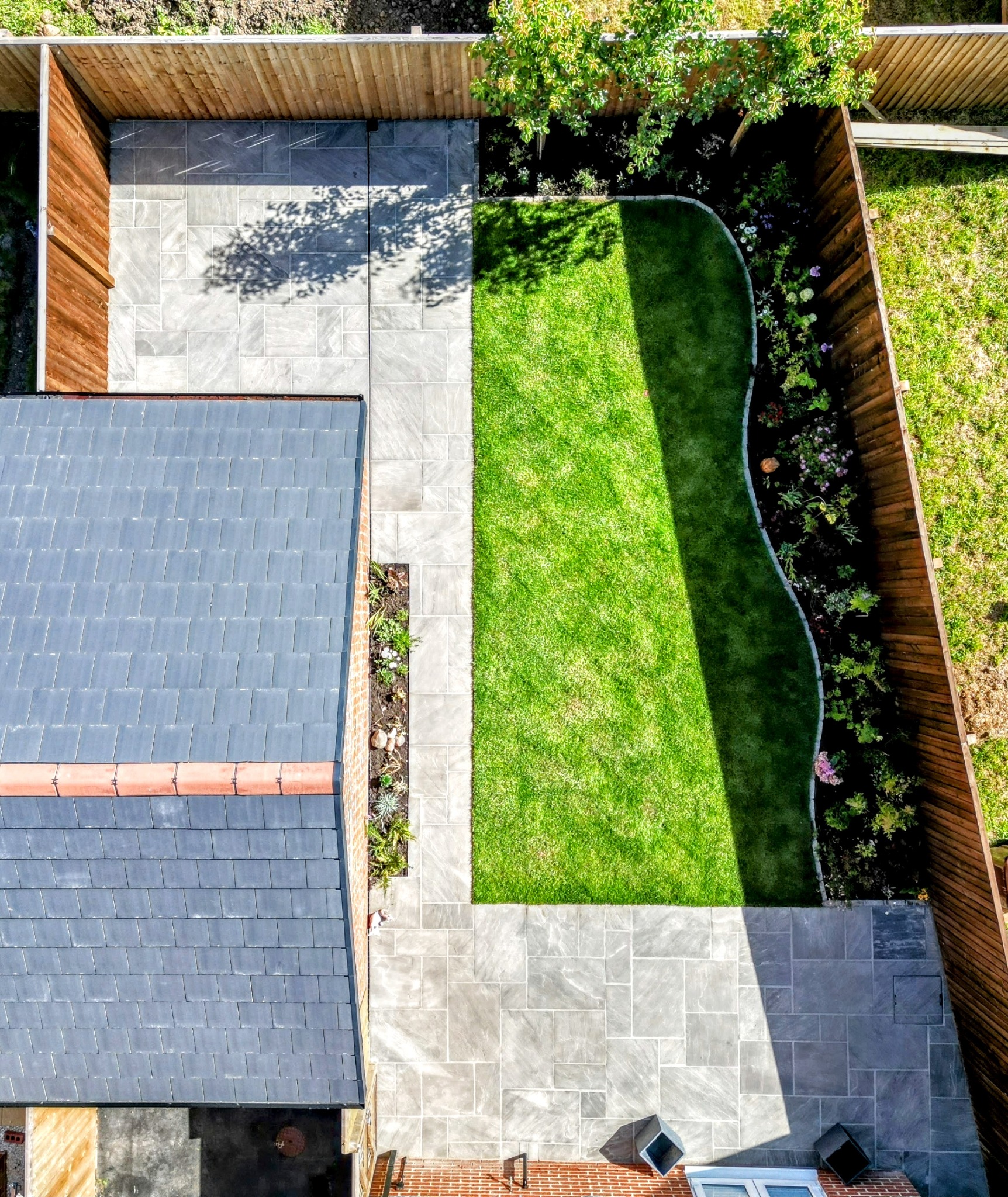 Aerial view of a landscaped garden with curved lawn, planted borders and stone paving