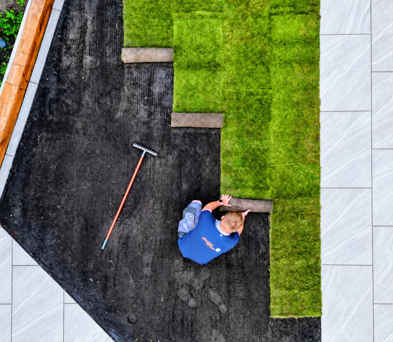 Laying fresh turf beside clean porcelain paving and timber sleepers